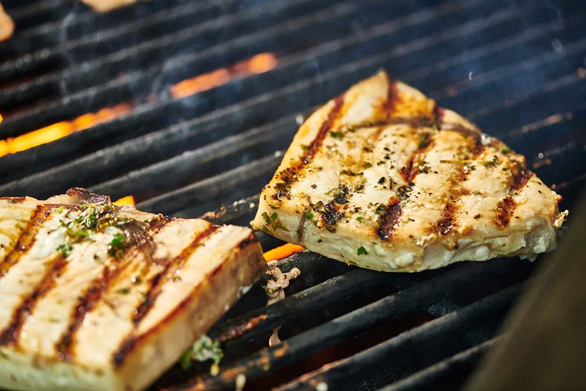 Two swordfish steaks over flames on hot grill.