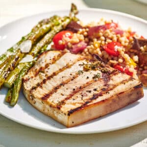 Plate of Grilled Swordfish and sides on a white, wooden table.