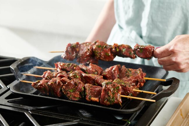 Woman placing Lamb Kebabs on a pan.