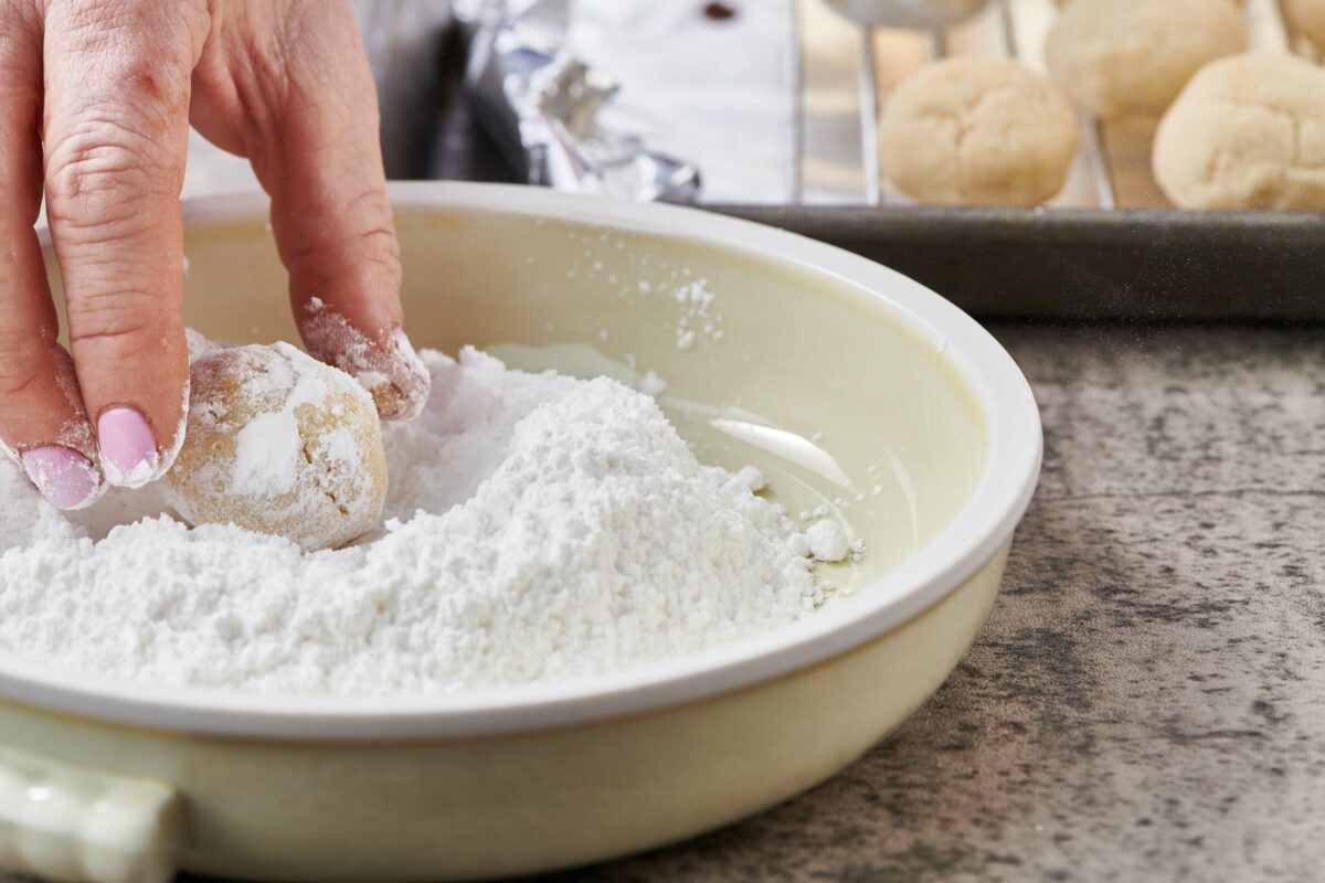 Woman dredging a Nut-Free Snowball Cookie in powdered sugar.