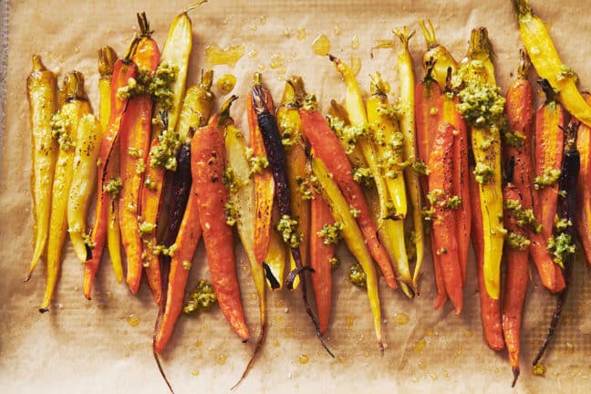 Roasted carrots in green olive dressing on parchment-lined baking sheet.