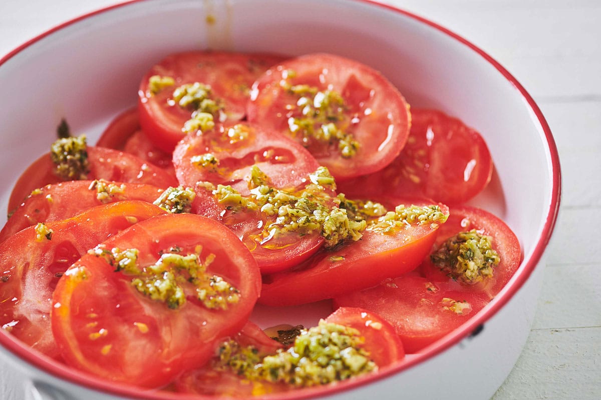 Sliced tomatoes with green olive dressing in white and red serving bowl.