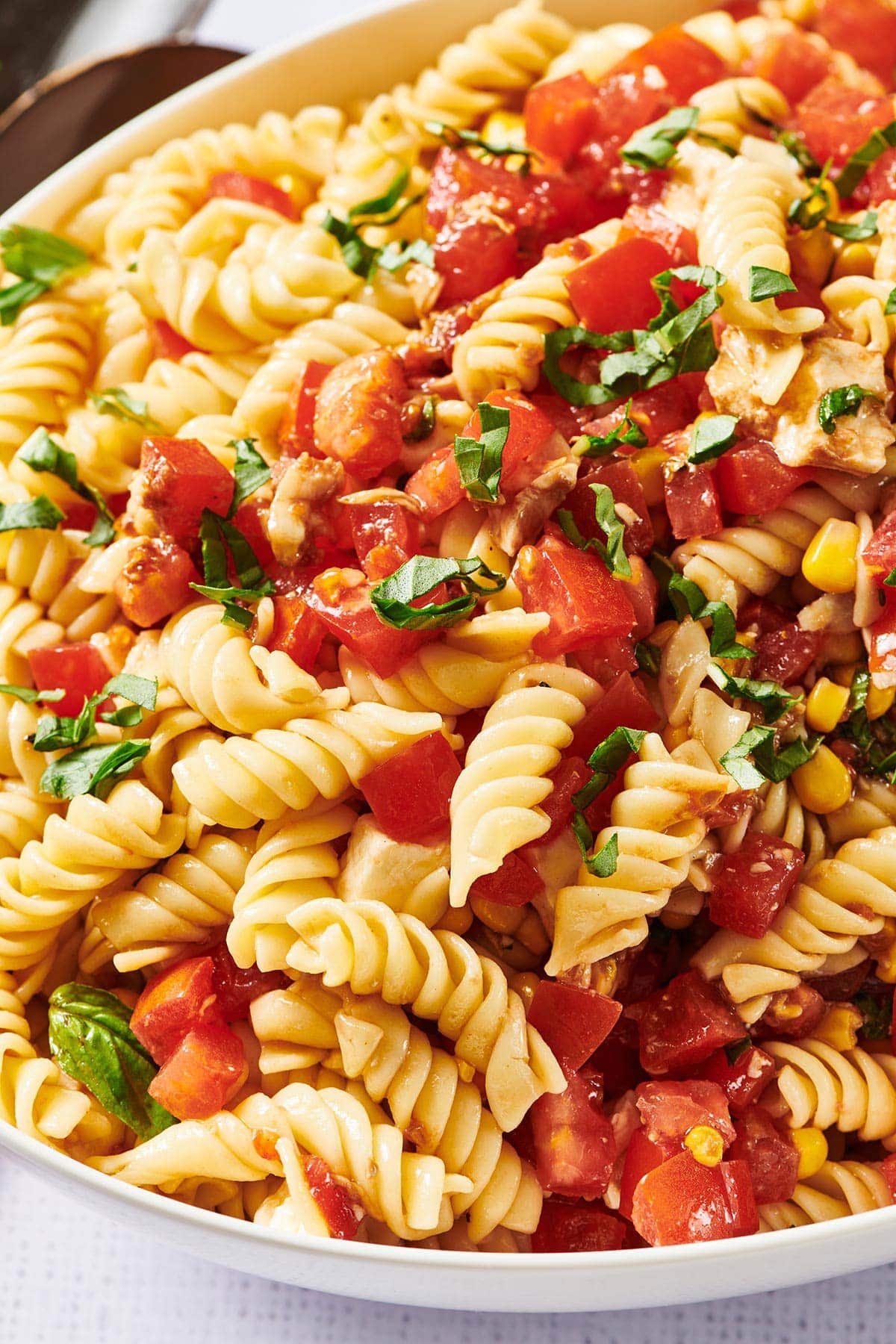 Pasta salad with fresh tomatoes, corn, and mozzarella in white serving dish.
