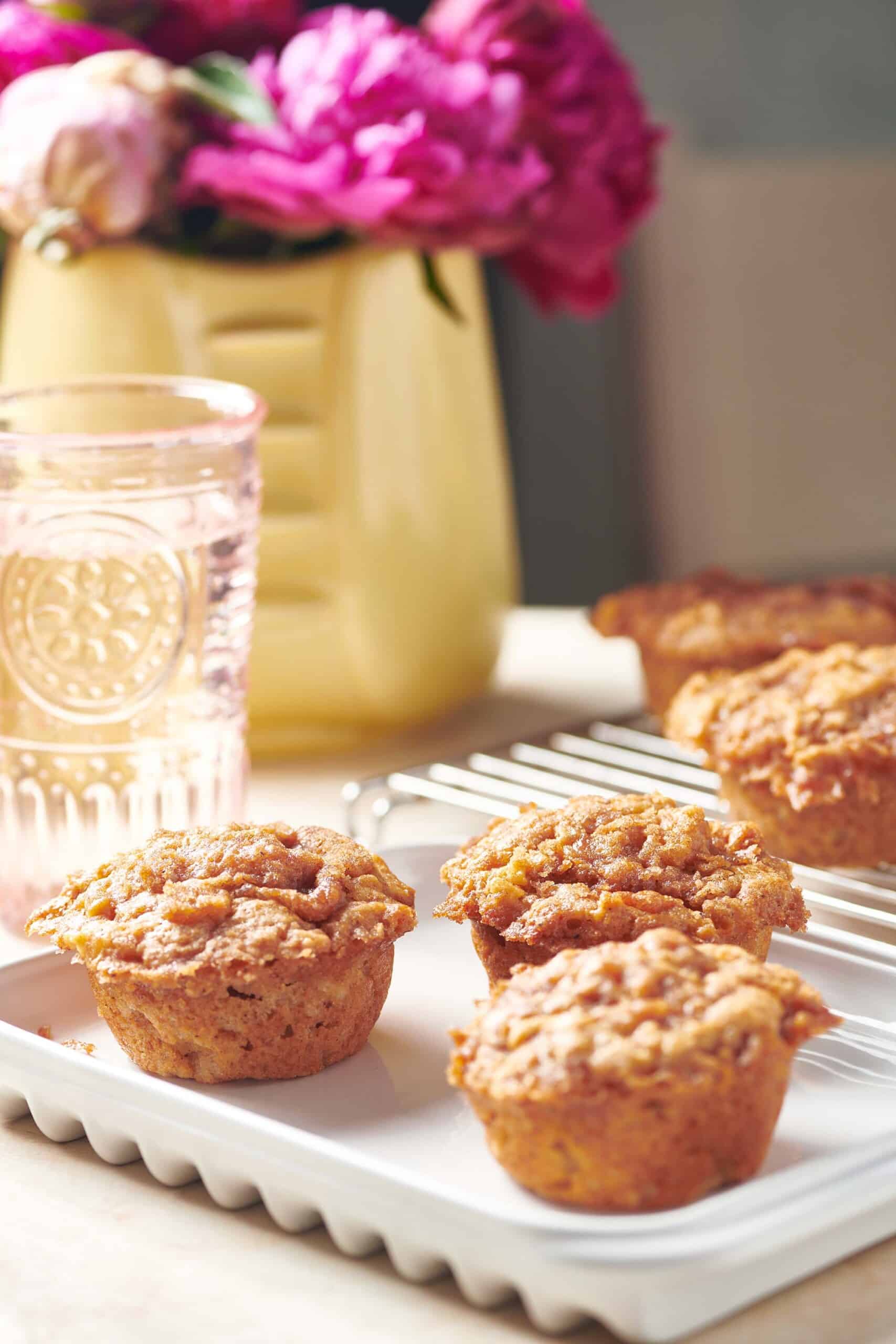 Brown Butter Apple Streusel Muffins on table with flowers and  a drink.