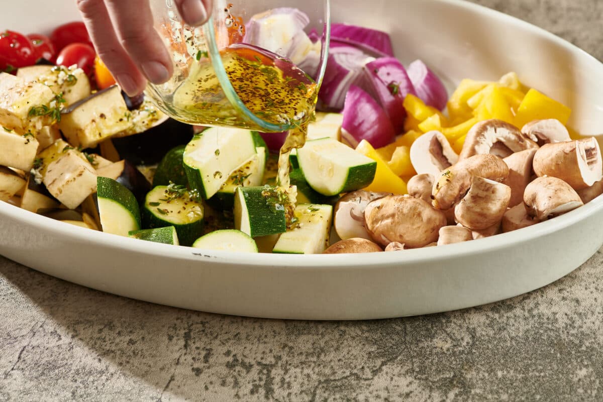 Pouring marinade over cubed veggies in large platter.