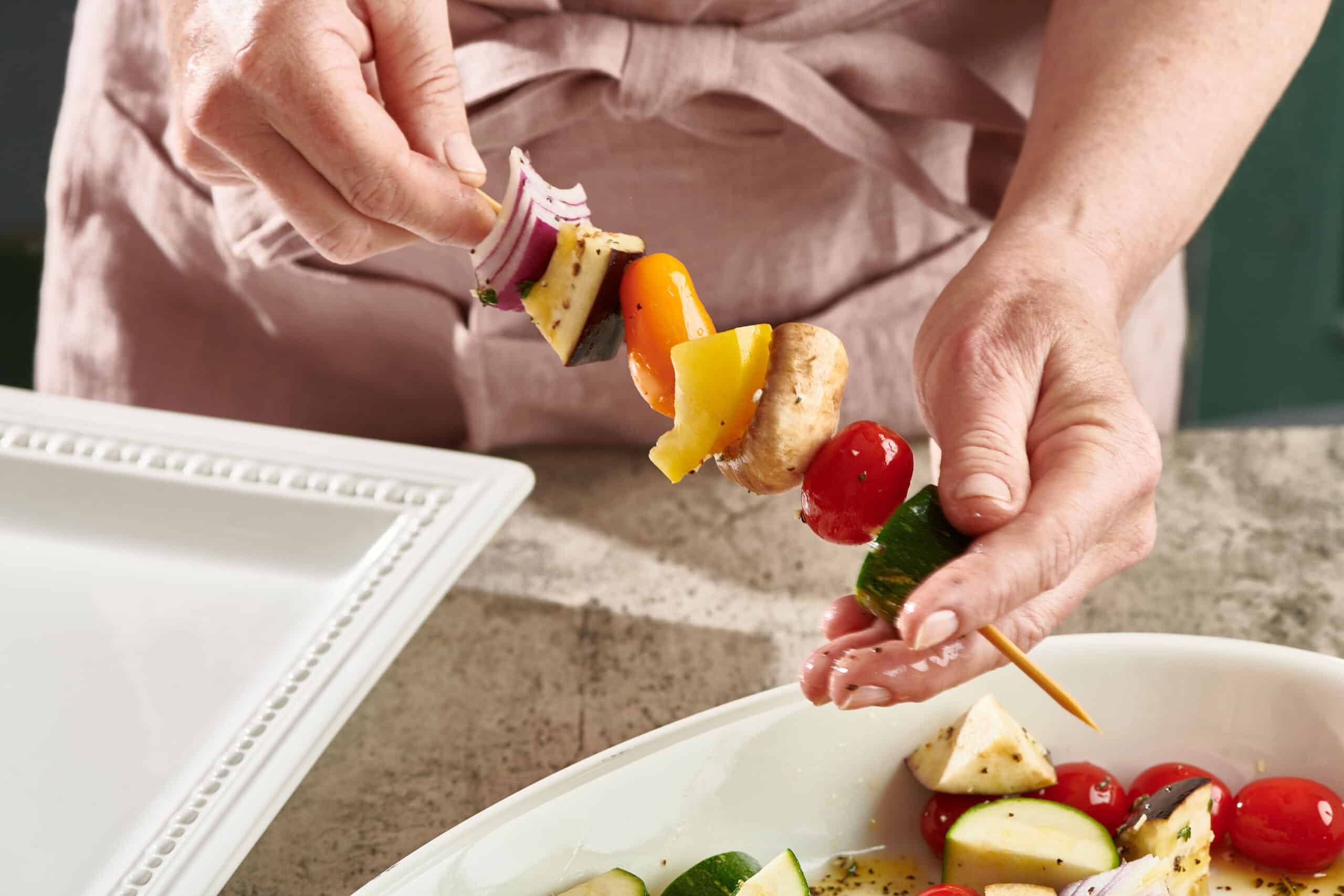 Woman adding cut vegetables to wooden skewer.