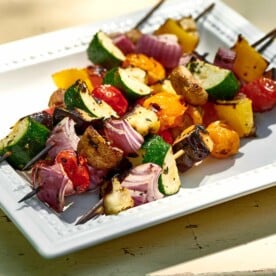 Grilled vegetable kebabs on white plate.