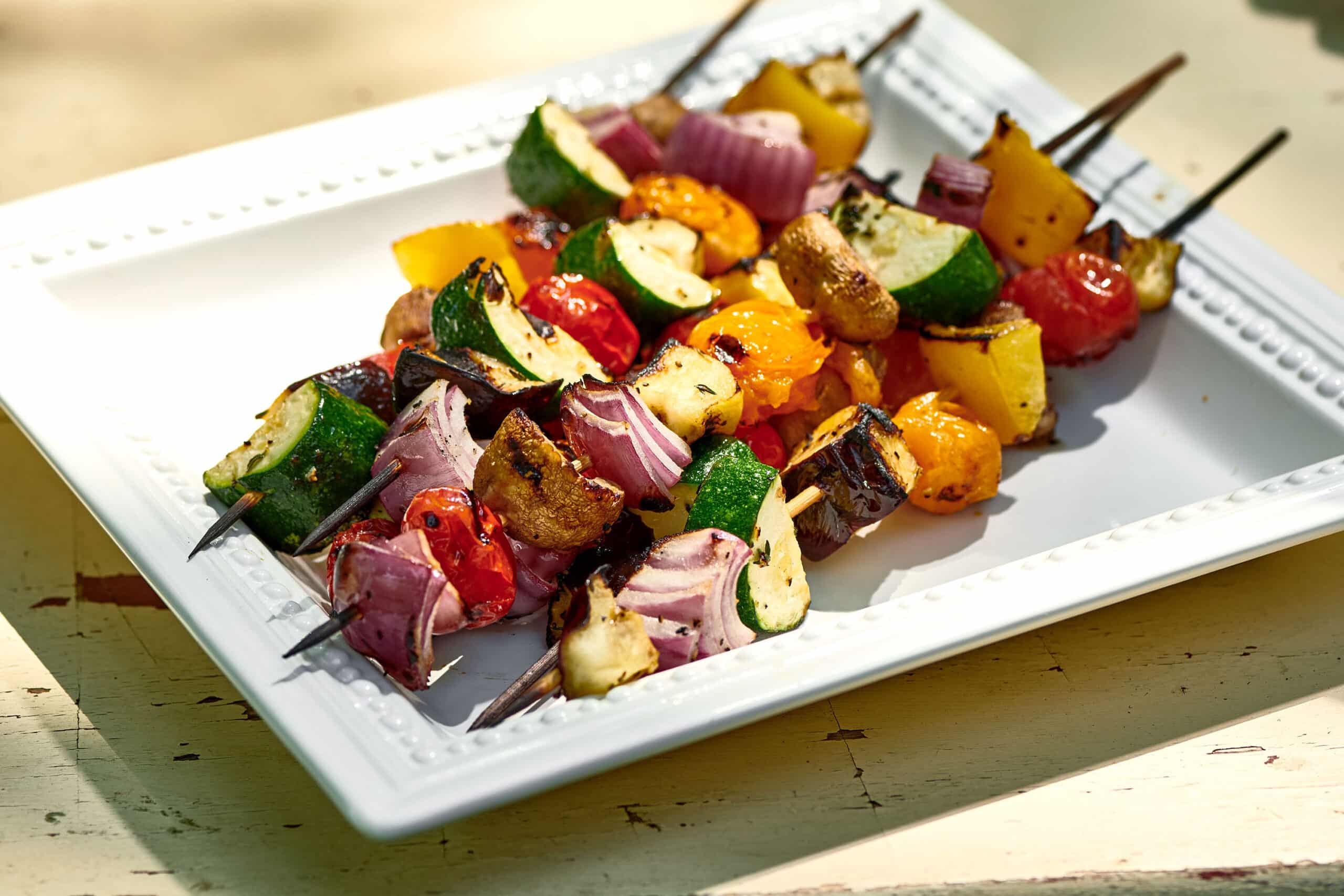 Grilled vegetable kebabs on white plate.