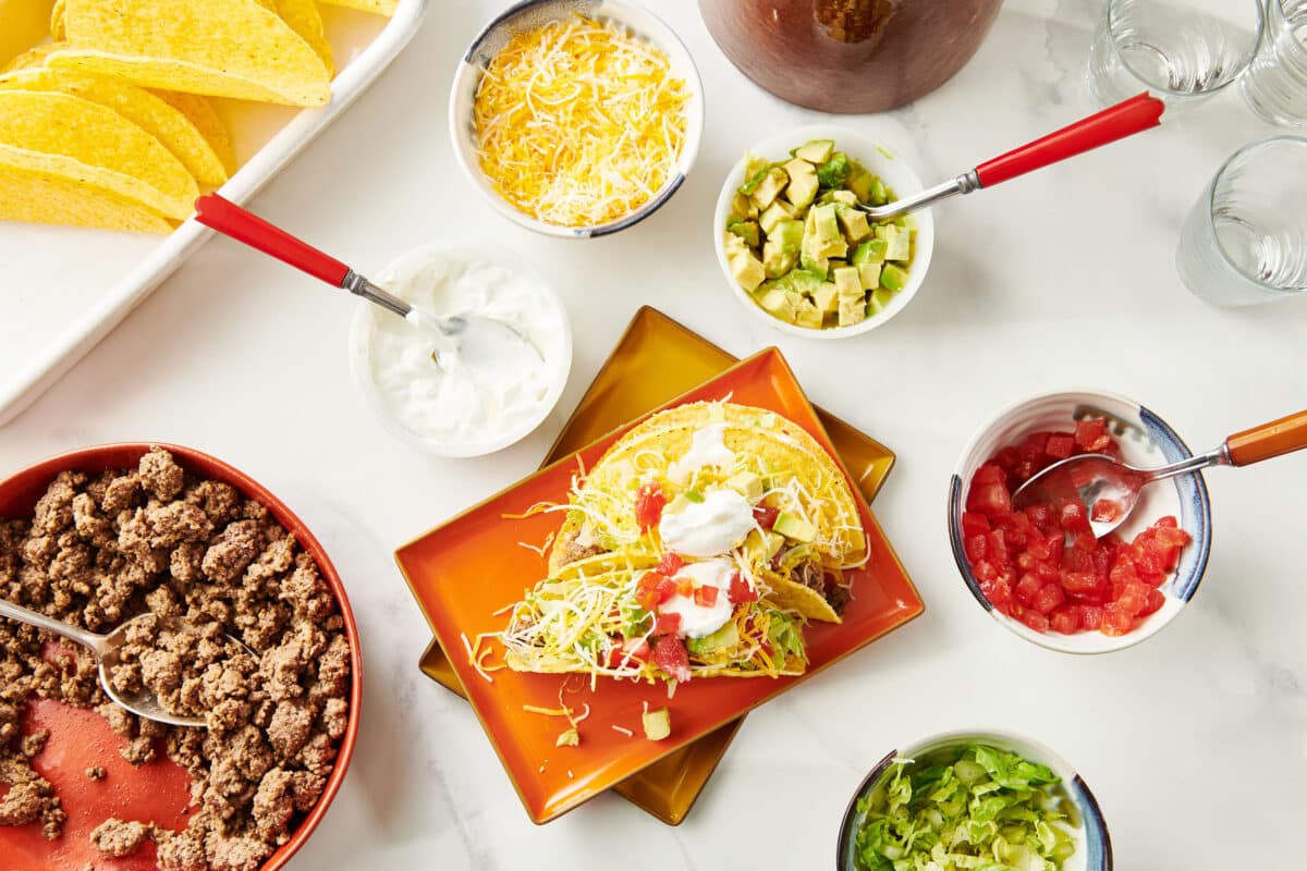 Ground Beef Tacos on a plate surrounded by bowls of taco toppings.