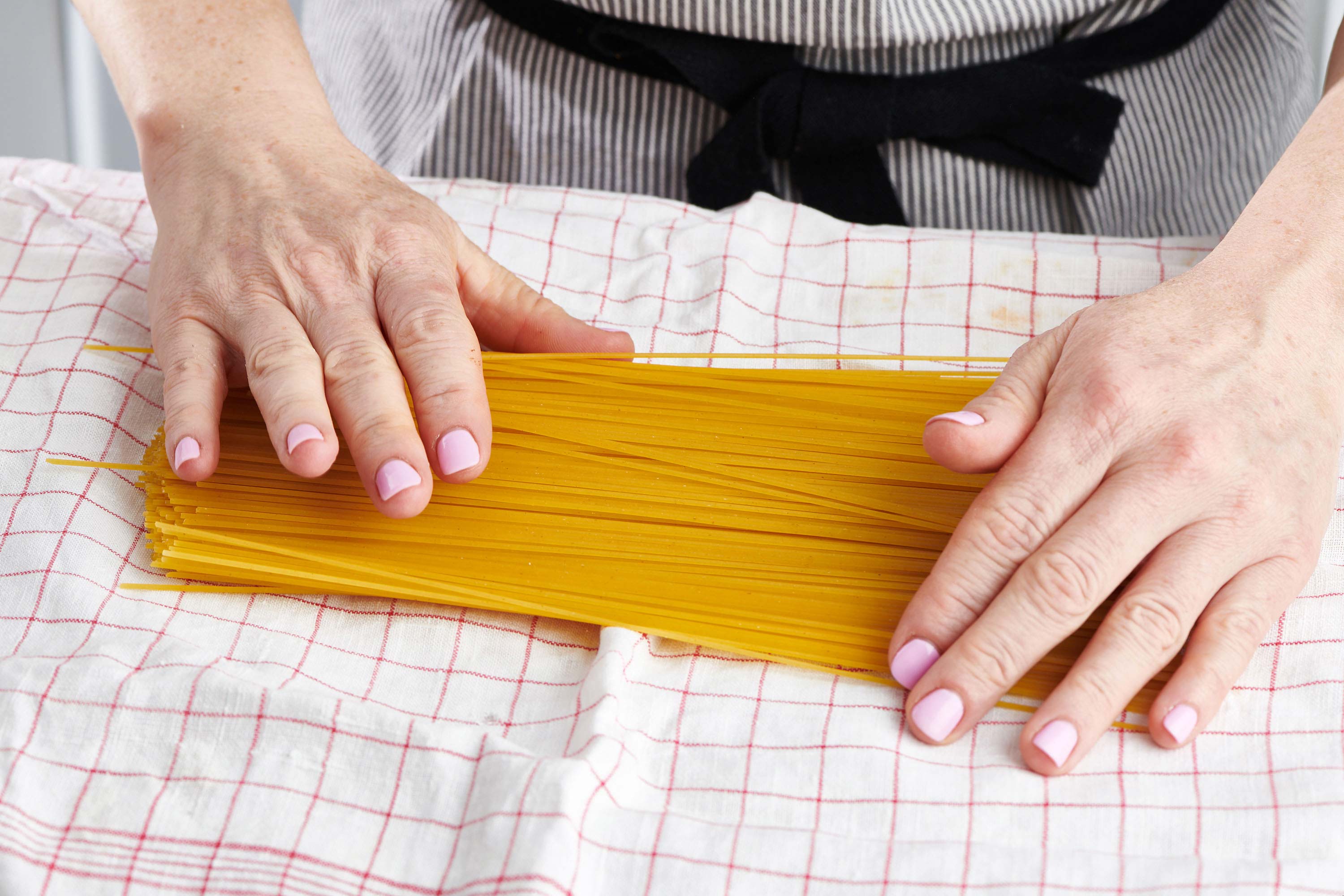 Woman placing uncooked spaghetti on a clean dishtowel.