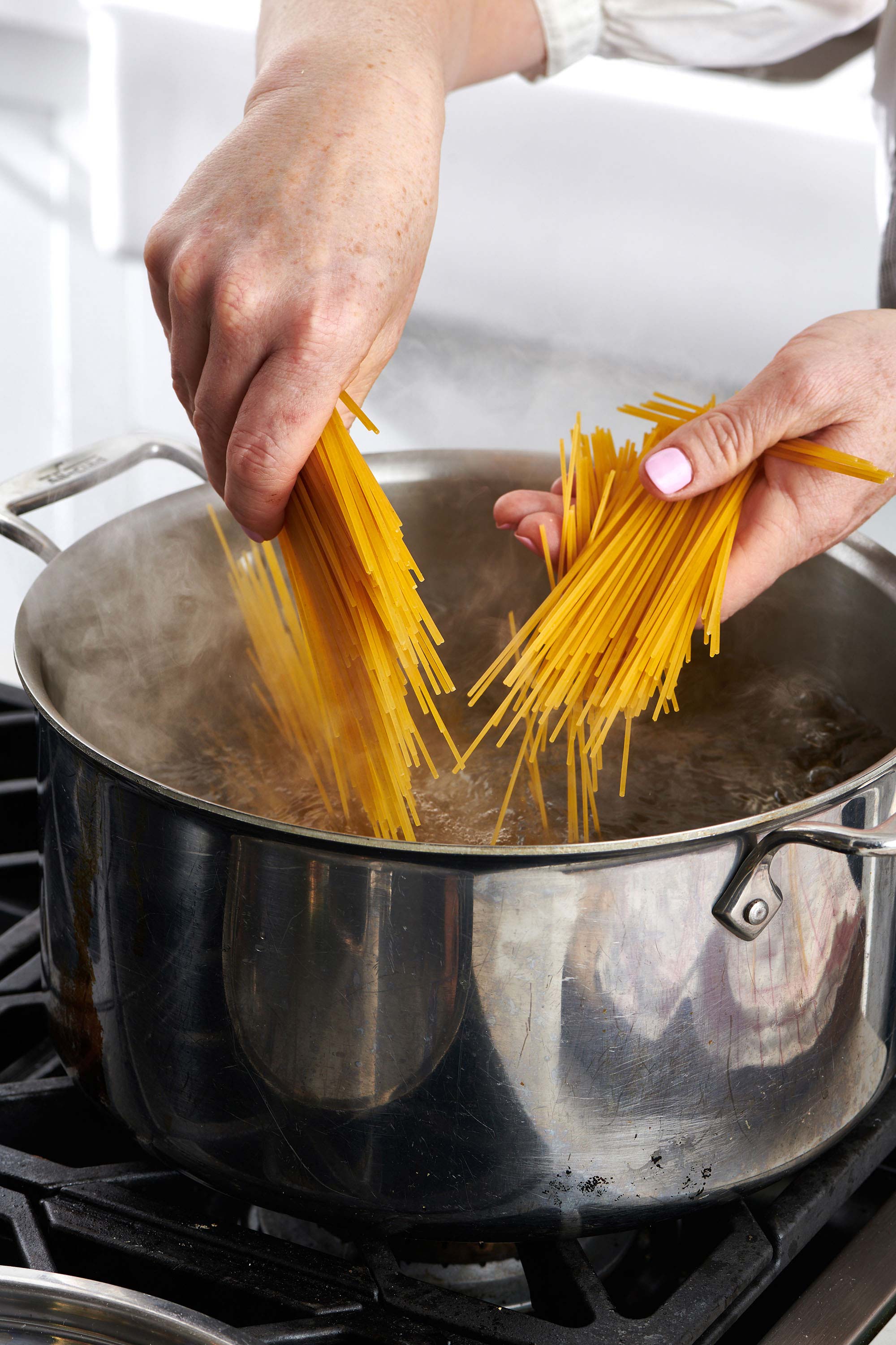 Woman placing broken dried spaghetti into pot of boiling water.