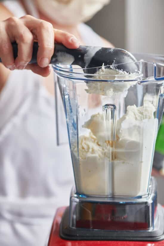 Ice cream scoop dropping ice cream into a blender.