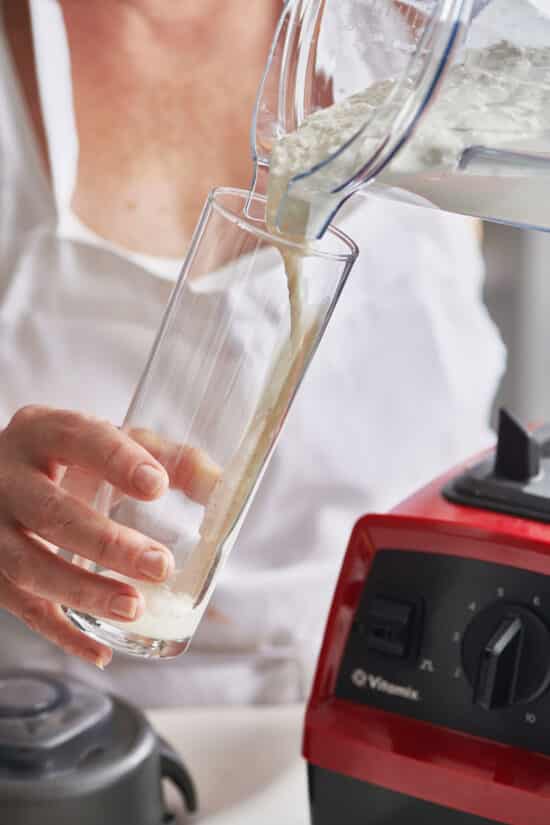 Woman pouring vanilla milkshake from a blender into a tall glass.