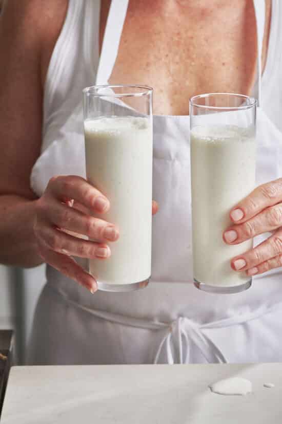 Woman holding two Vanilla Milkshakes in tall glasses.