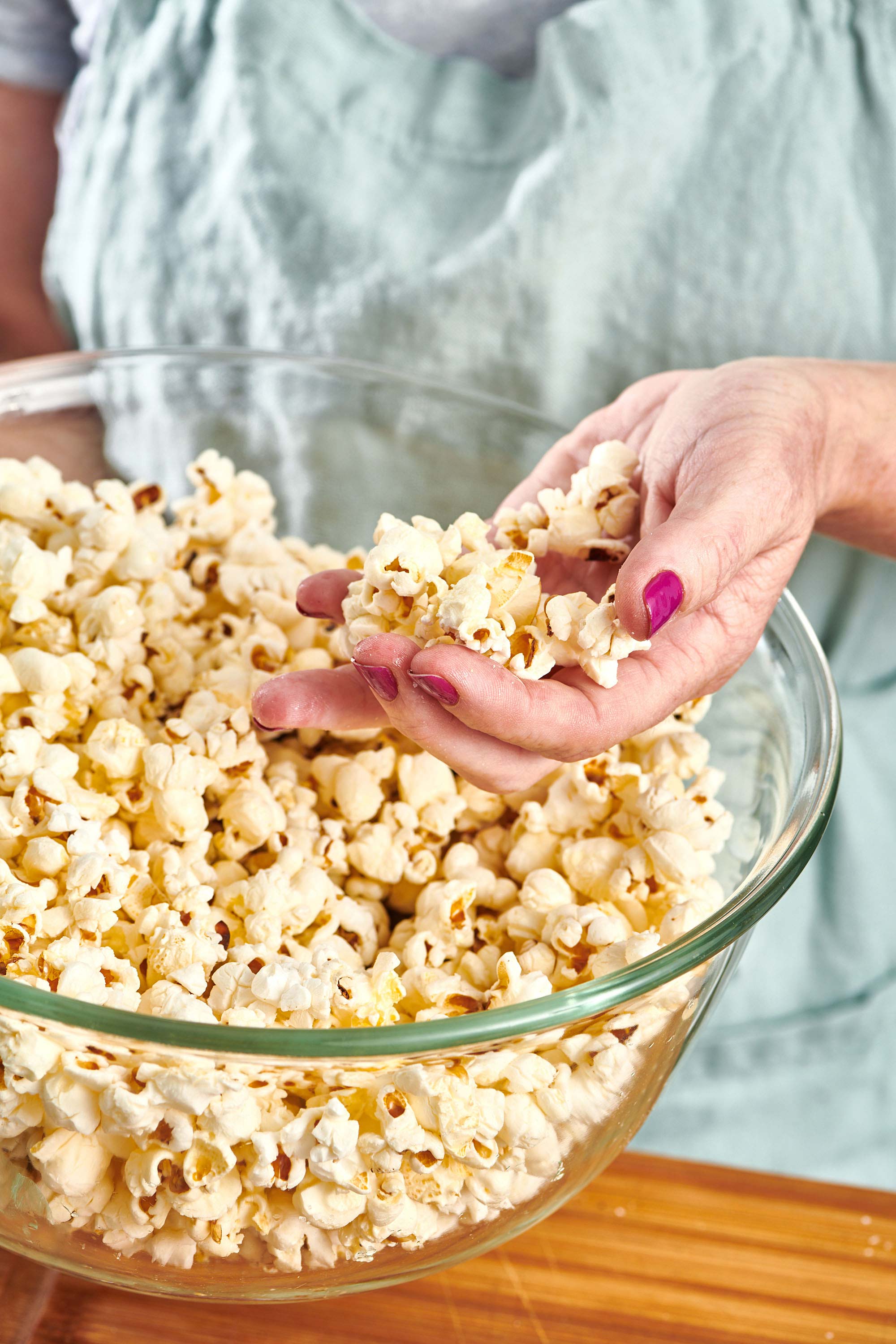 Woman holding a handful of popcorn over a bowl.