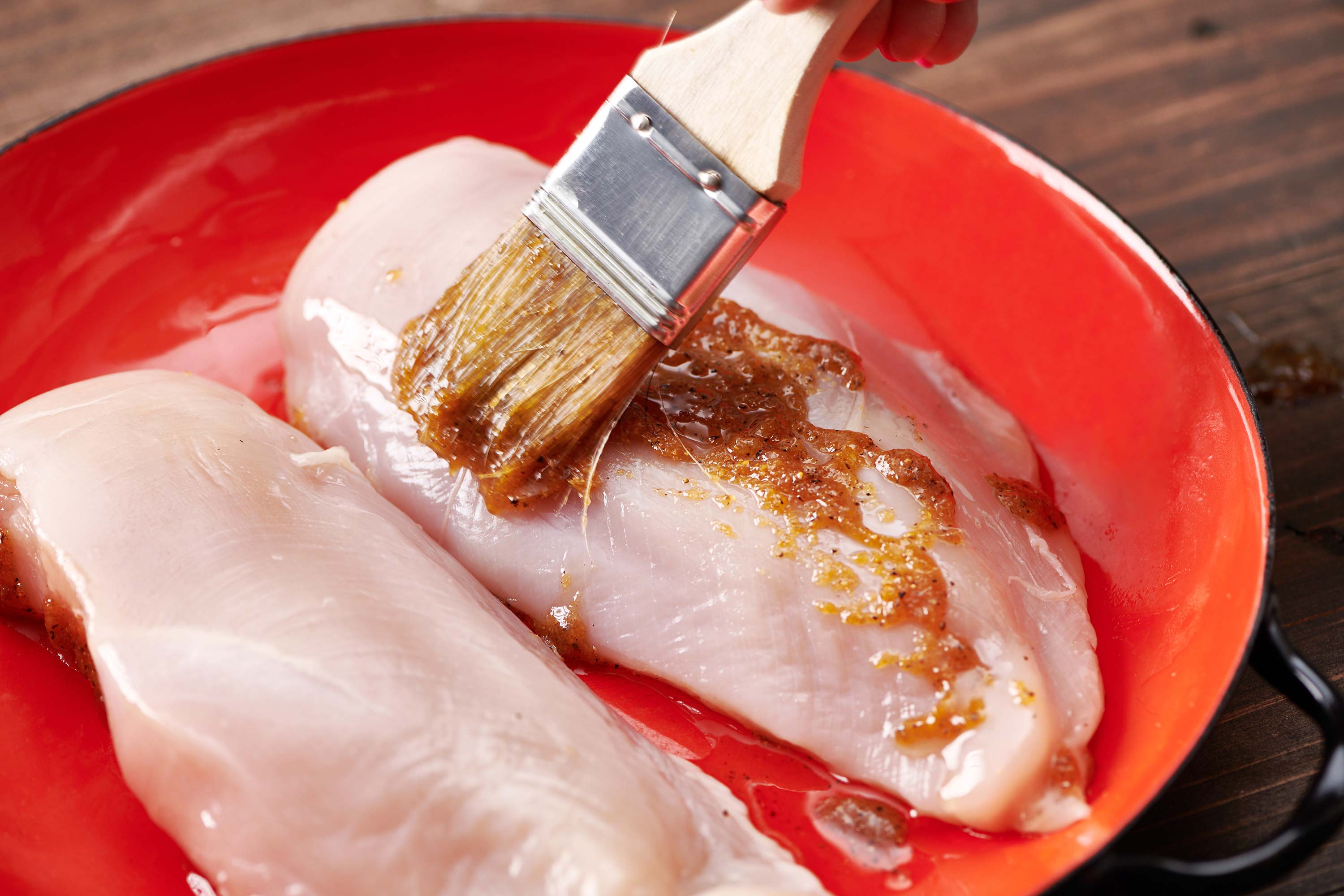 Basting chicken breasts with lemon pepper butter using a brush.