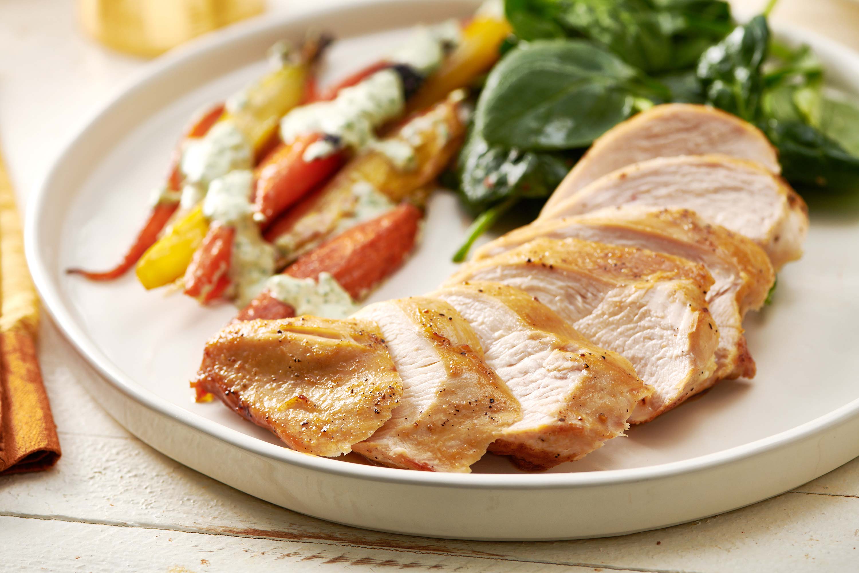 Sliced chicken on plate next to veggie sides.