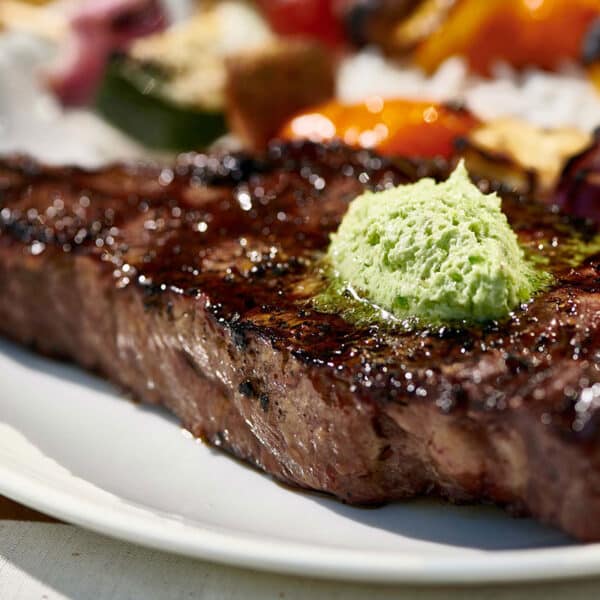 Grilled New York strip steak topped with jalapeno compound butter on white plate.