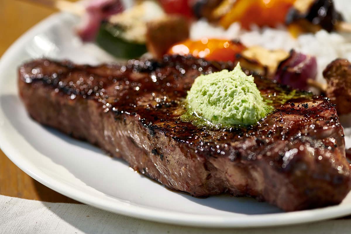 Grilled New York strip steak topped with jalapeno compound butter on white plate.