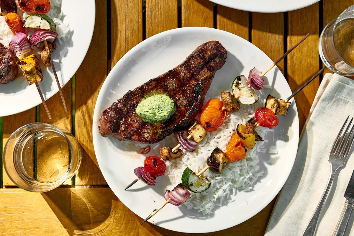 New York Strip Steak with Jalapeno Butter on a plate with kebabs and rice.