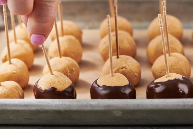 Woman placing a chocolate-dipped Buckeye Ball onto a lined baking sheet.