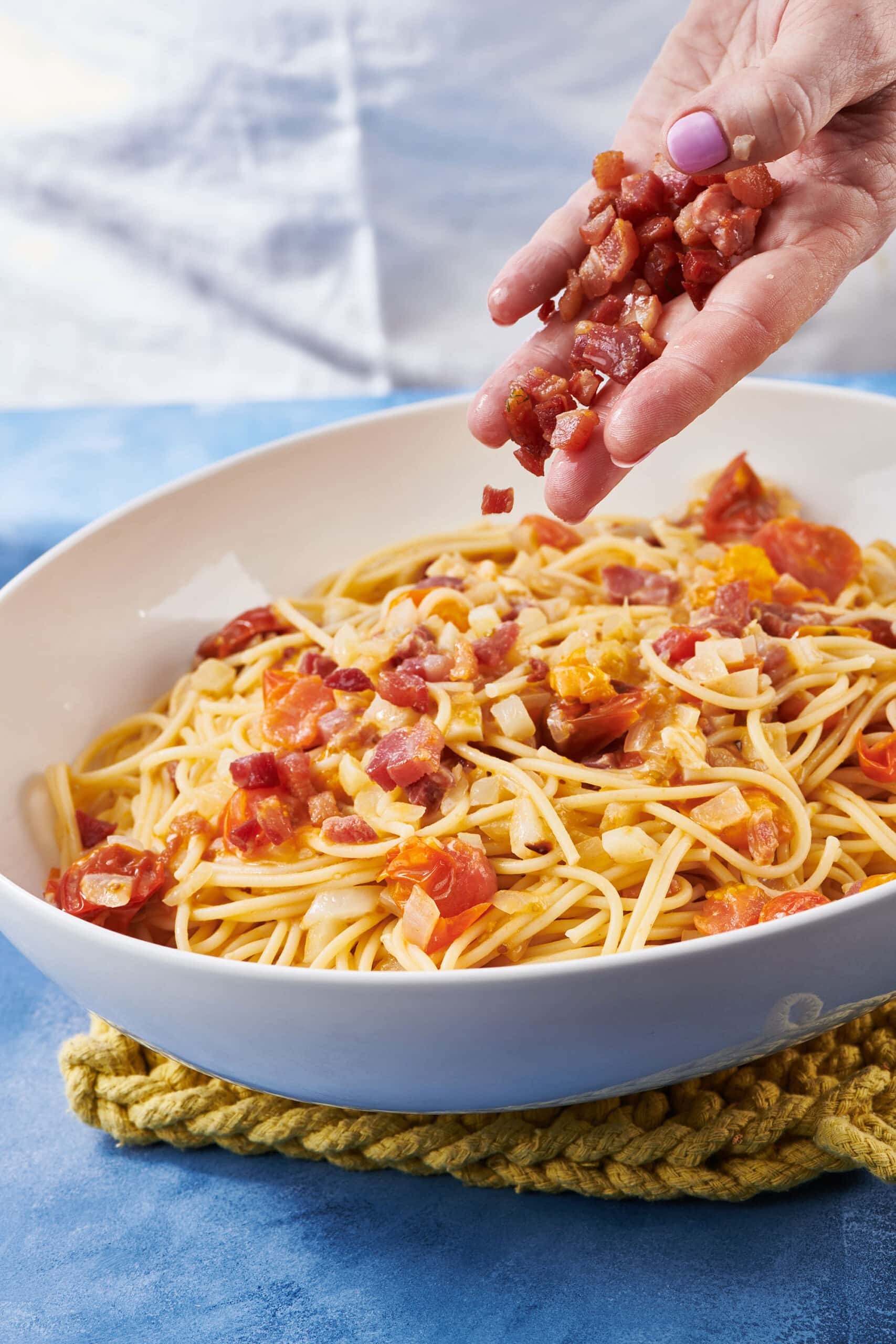 Woman sprinkling pancetta onto a bowl of pasta.
