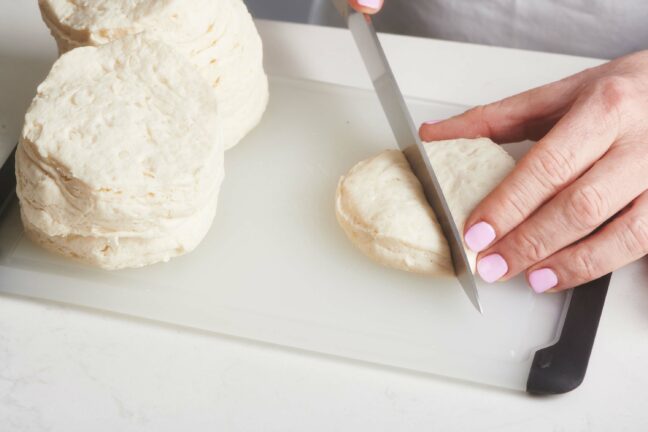 Woman slicing rounds of biscuit dough.