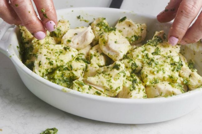 Woman mixing dough and pesto mixture in a white bowl.