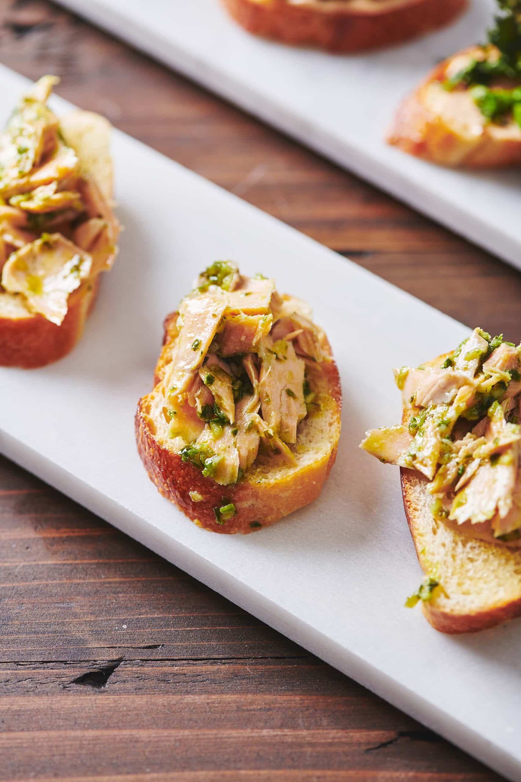 Salmon Crostini with Chimichurri Sauce on a long white plate.