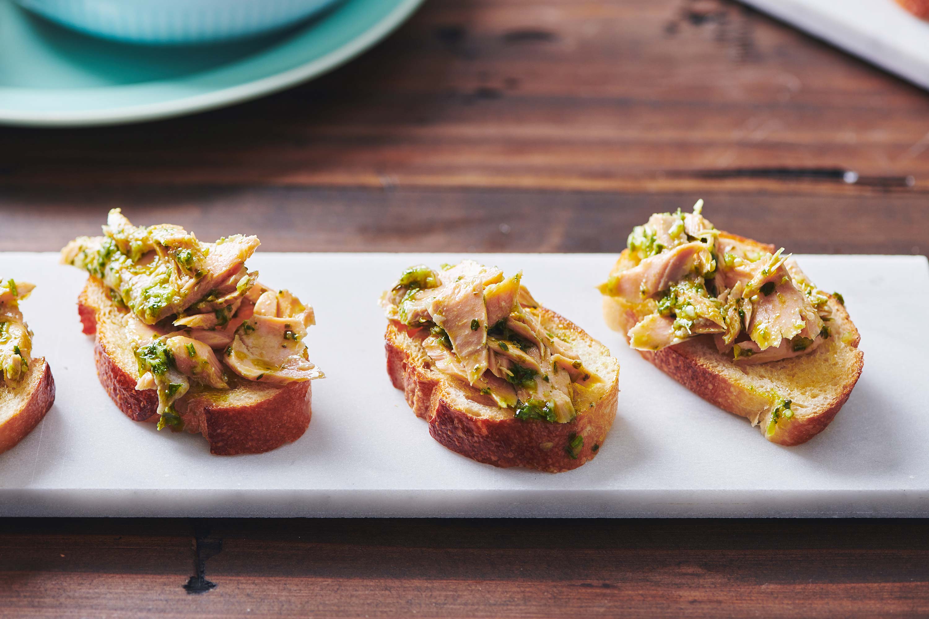 Line of Salmon Crostini with Chimichurri Sauce on a white plate.