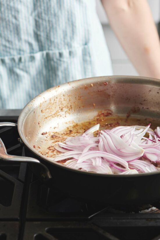Sautéing sliced red onions in pan on the stove.