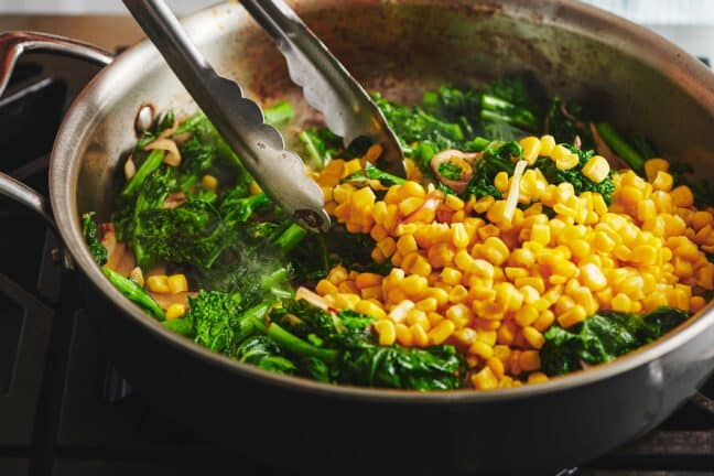 Mixing Sauteed Broccolini and Corn in a pan with metal tongs