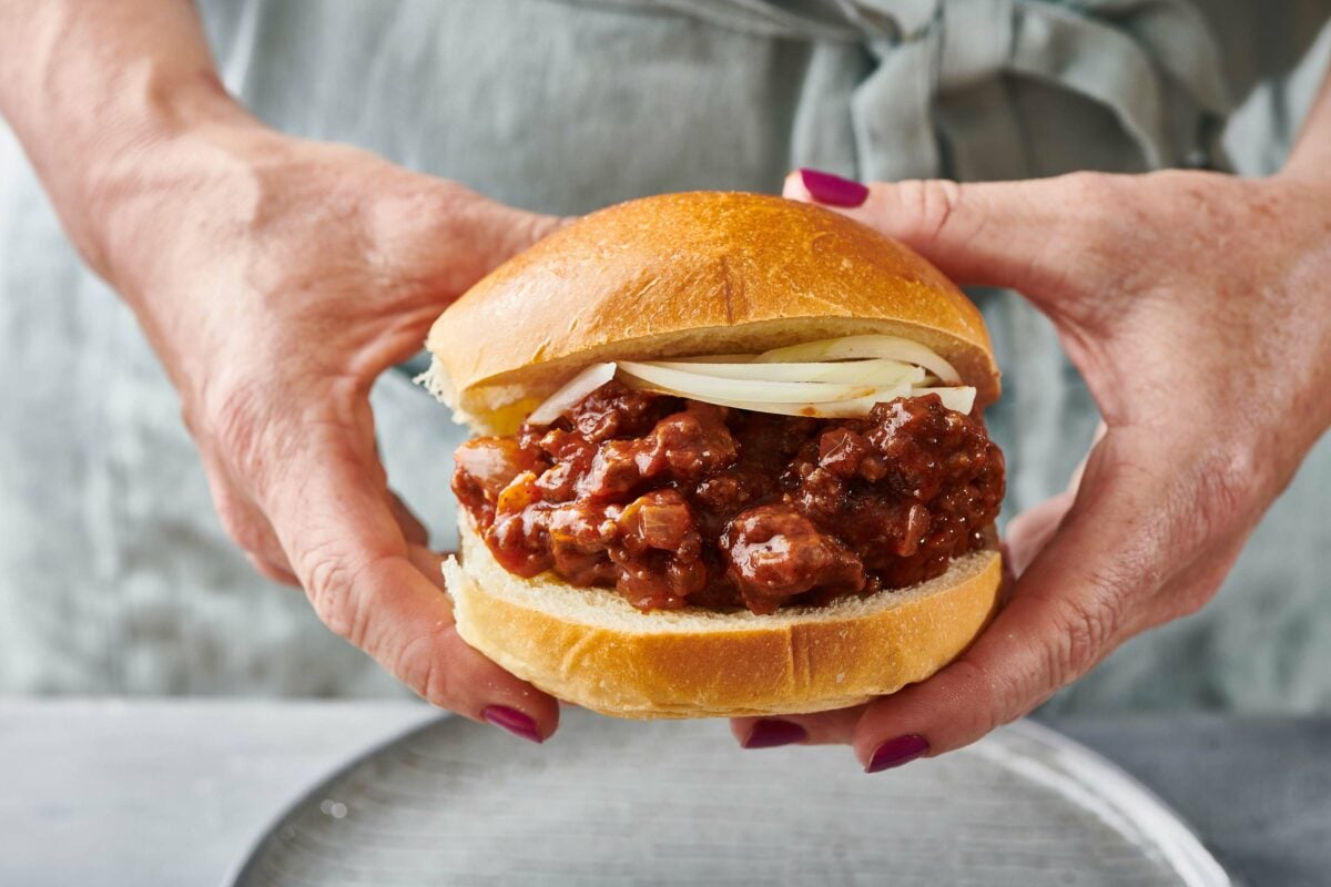 Woman holding a Sloppy Joe with onions.