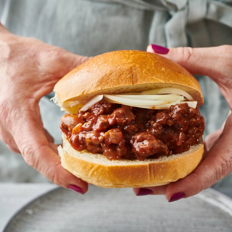 Woman holding a Sloppy Joe with onions.