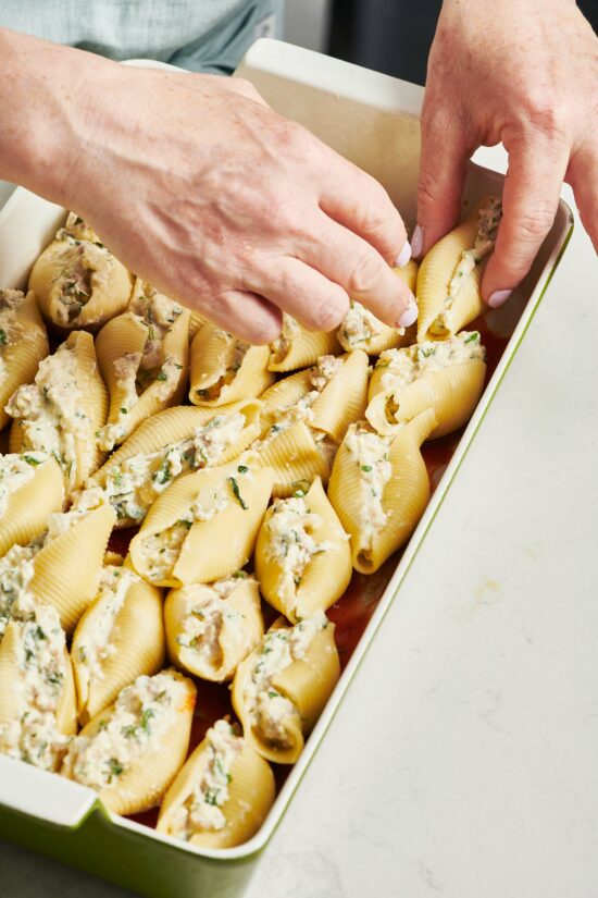 Woman arranged stuffed pasta shells in a baking dish.