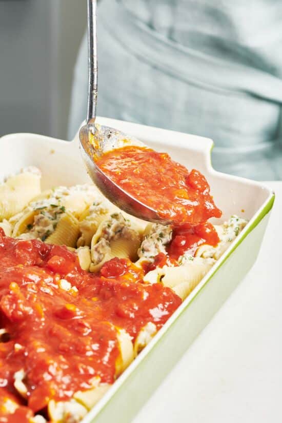 Ladle putting red sauce on a baking dish of Stuffed Shells.
