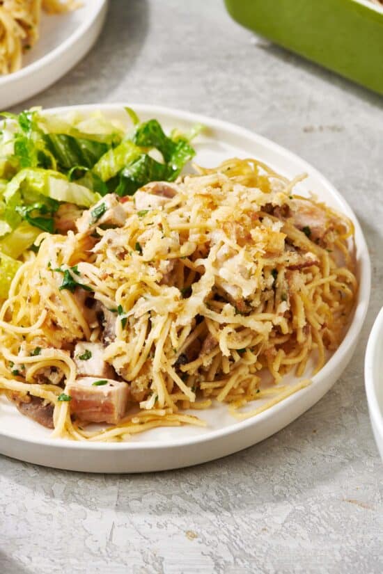 Turkey Tetrazzini topped with parmesan cheese on a plate with salad.