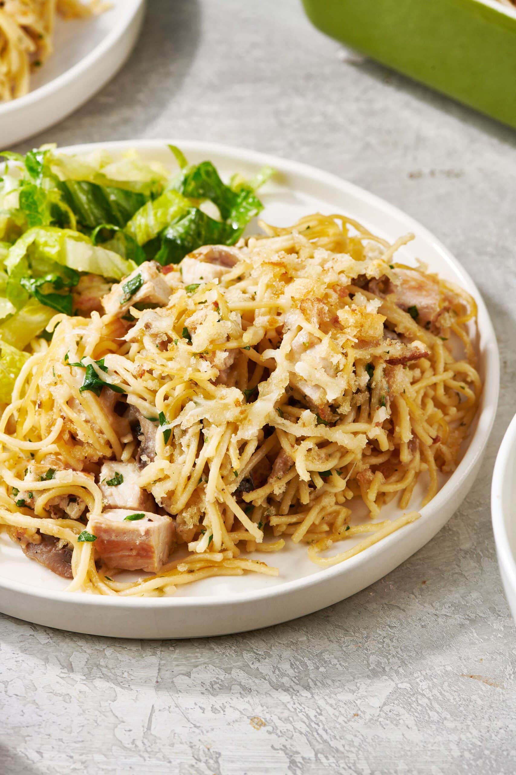 Turkey Tetrazzini topped with Parmesan cheese on a plate with salad.