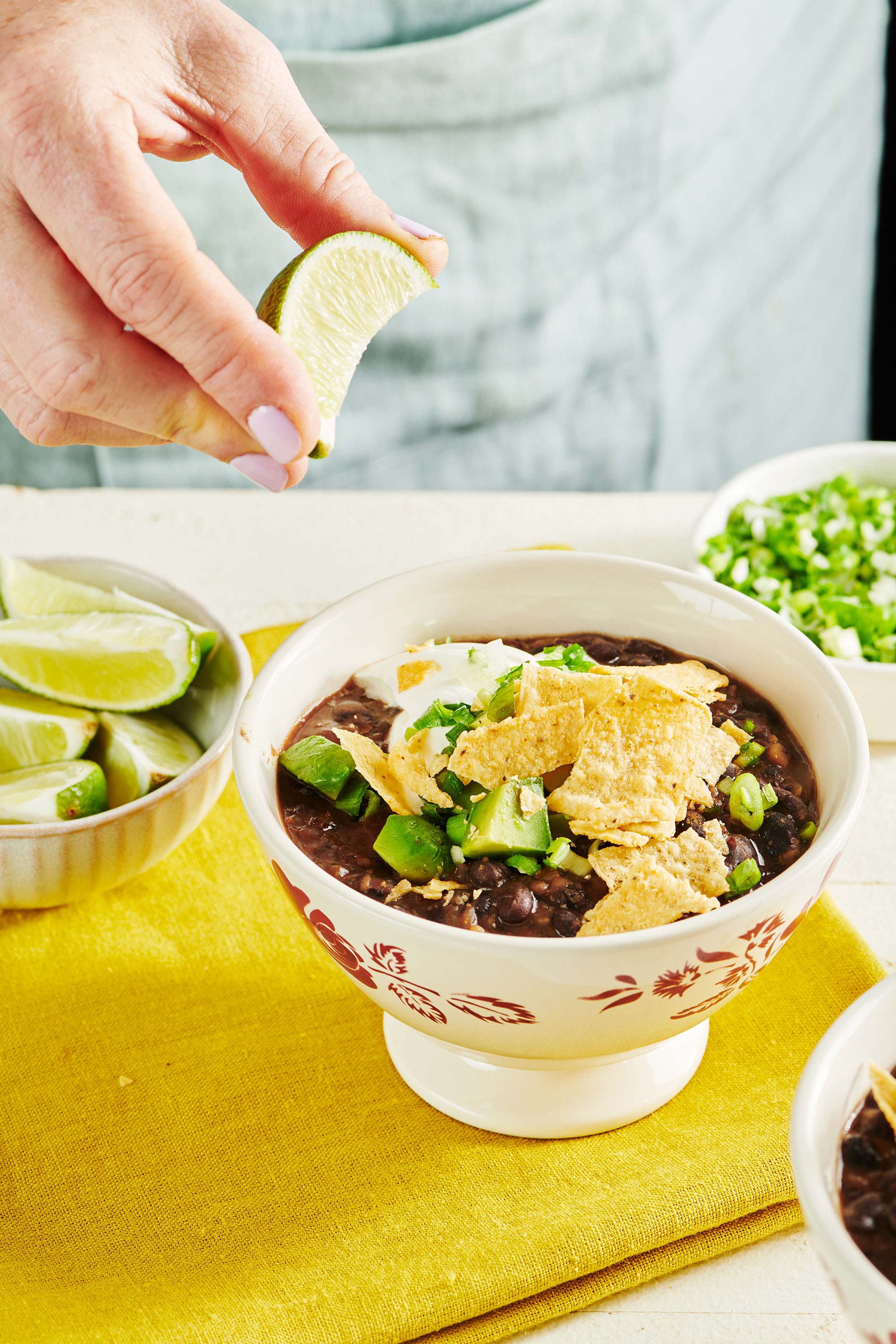 Woman squeezing a lime slice onto a bowl of Vegetarian Black Bean Soup.