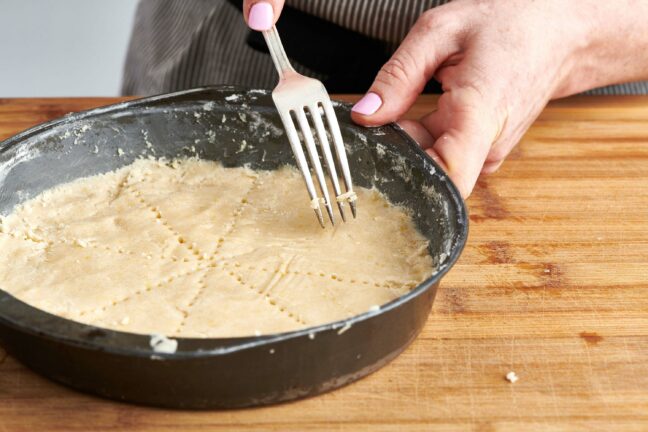 Woman scoring shortbread cookie dough with a fork.