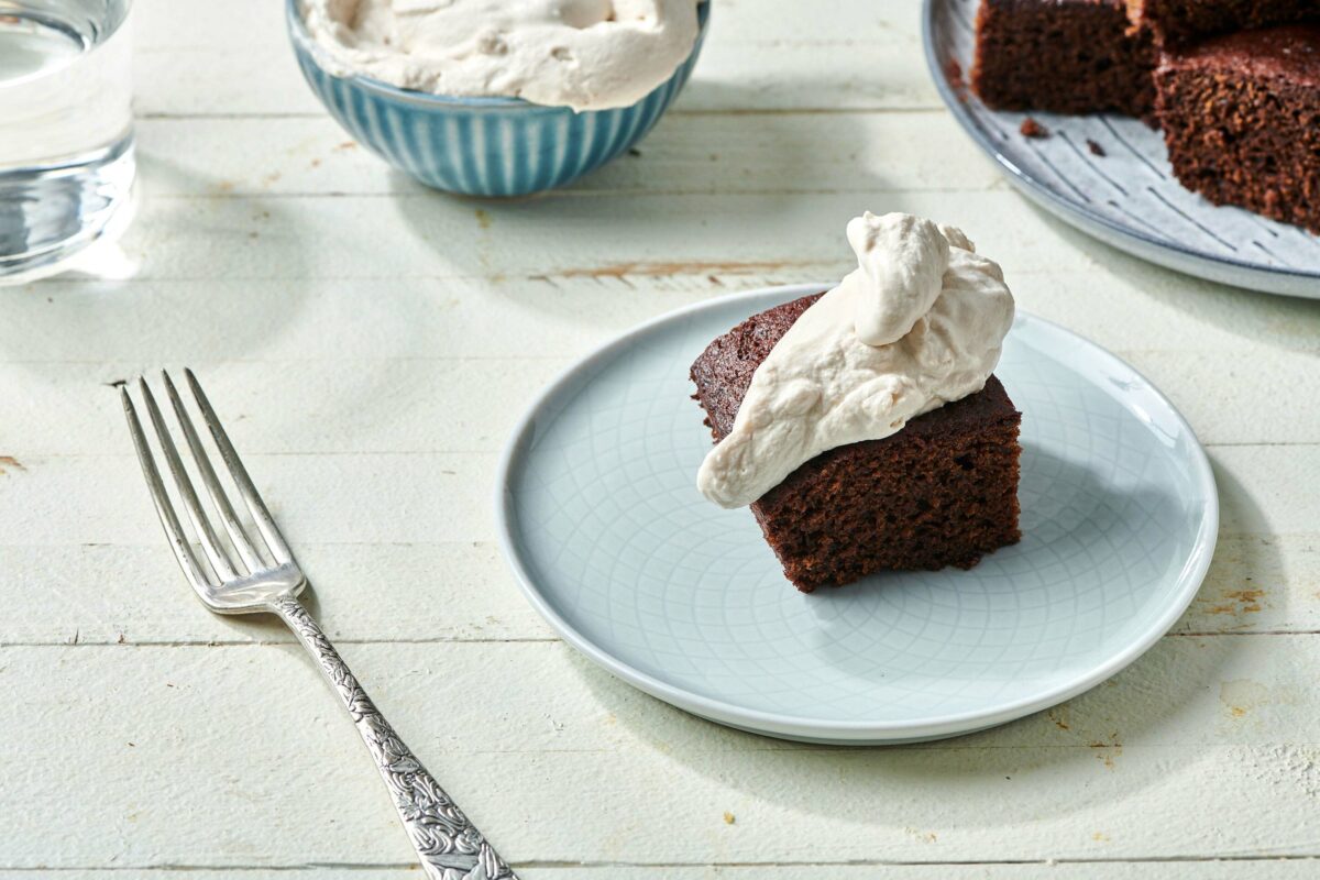 Piece of Gingerbread Cake topped with whipped cream on a plate.