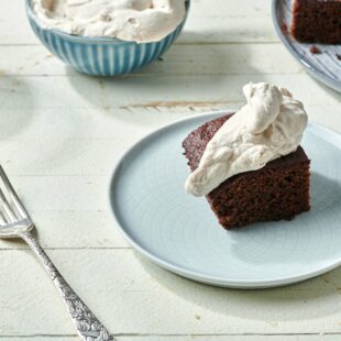 Piece of Gingerbread Cake topped with whipped cream on a plate.