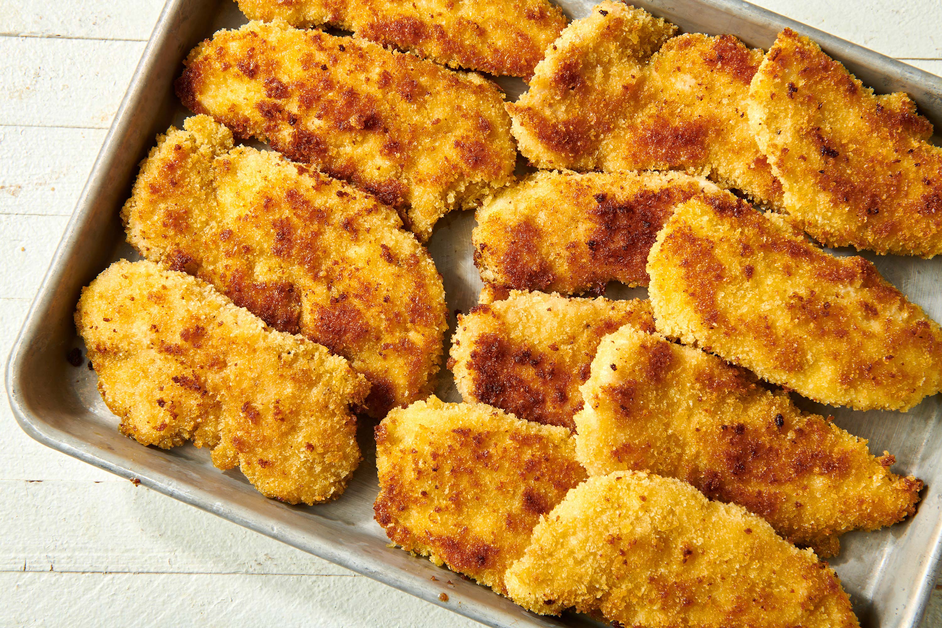 Baking sheet piled with breaded homemade Chicken Tenders.