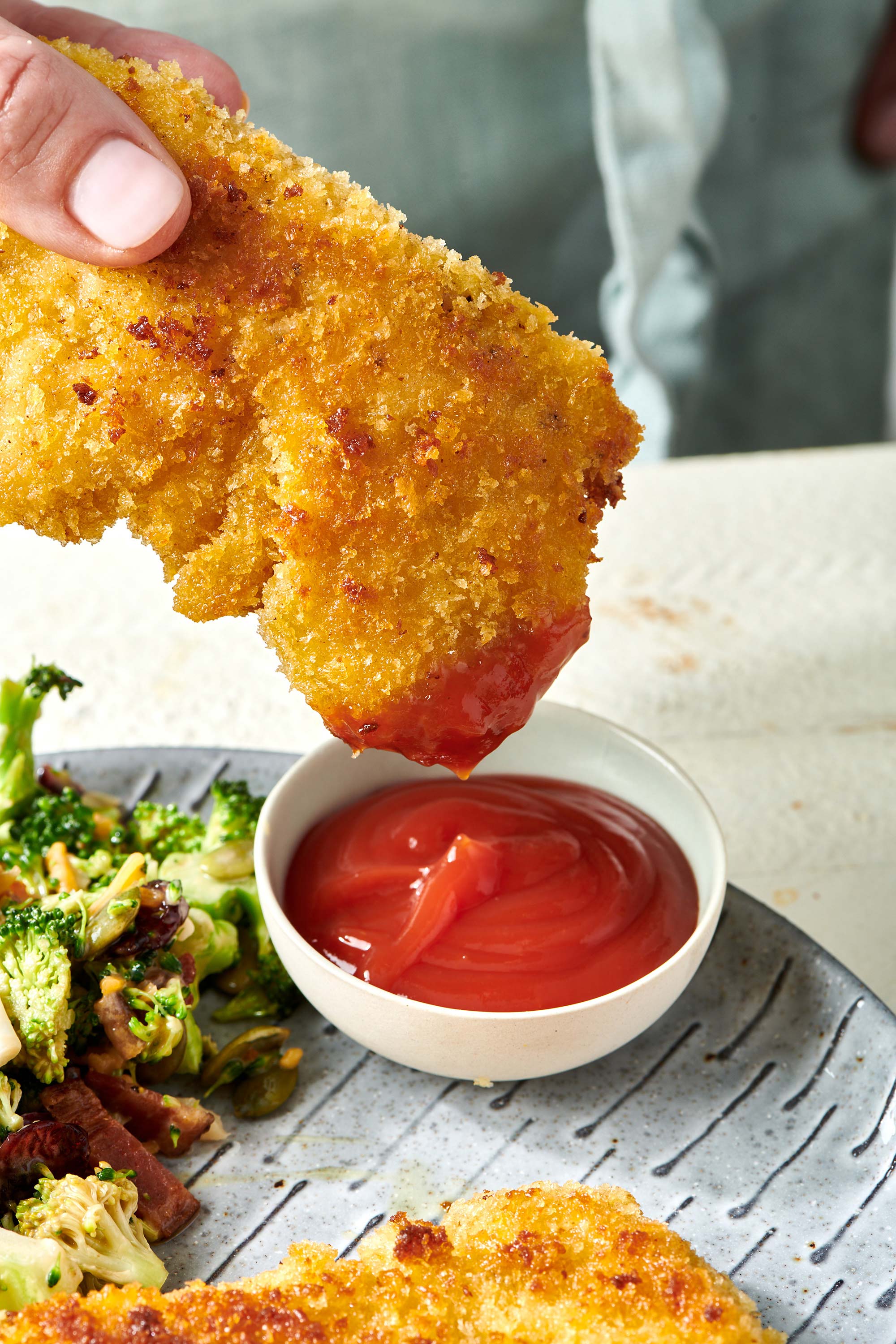 Dipping breaded chicken tender into small bowl of ketchup.