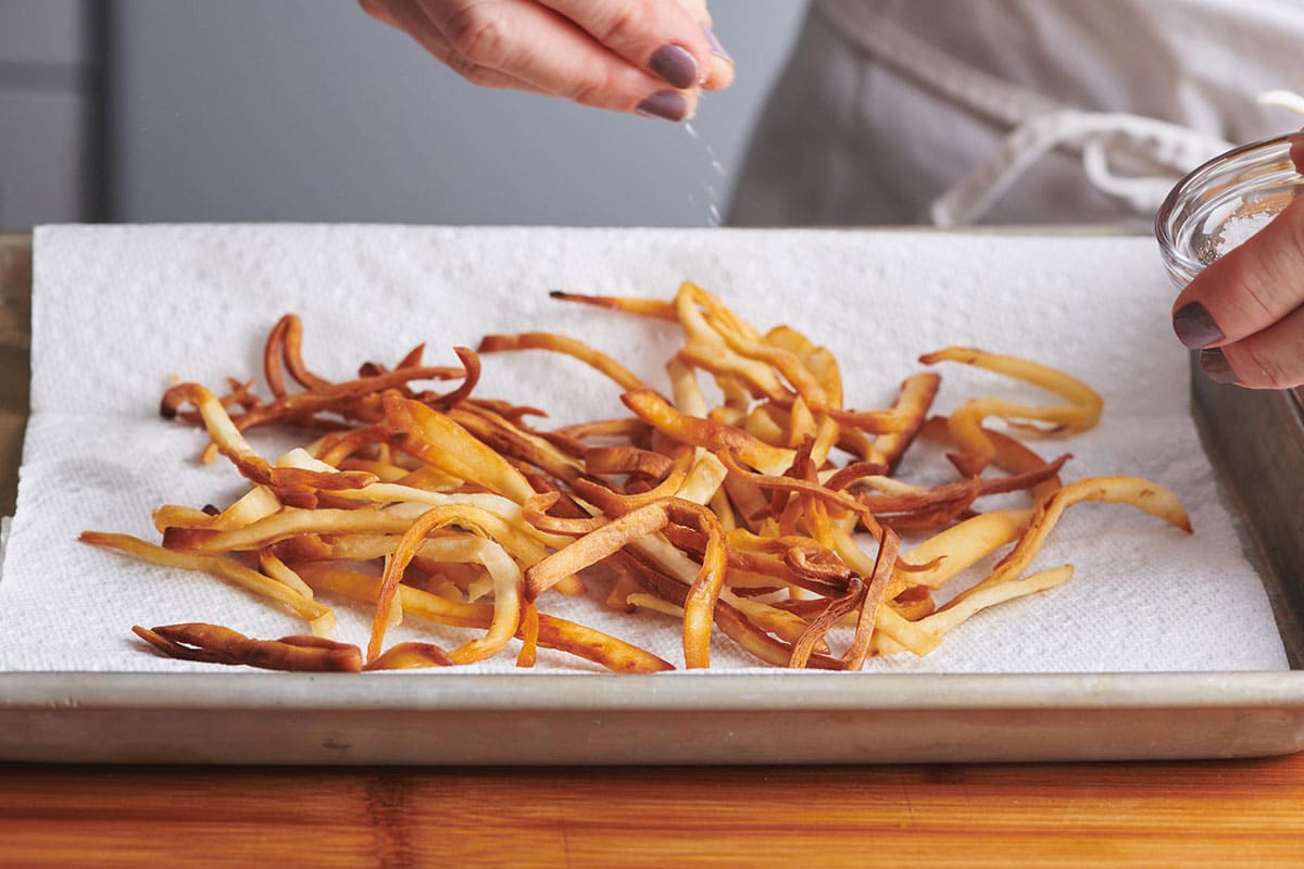 Woman salting tortilla strips on paper towel.