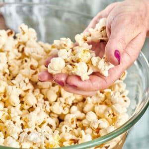 Woman with handful of popcorn over large bowl.