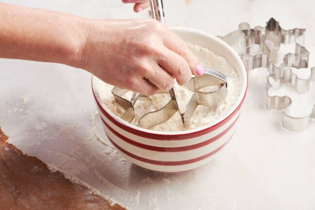 Woman dipping a person-shaped cookie cutter into flour.