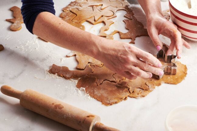 Woman cutting gingerbread dough with a snowflake-shaped cookie cutter.