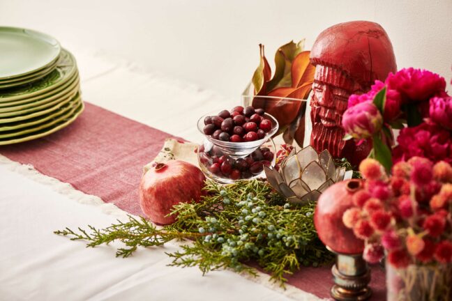 Red table runner topped with greenery, flowers, fruit, and decorations.
