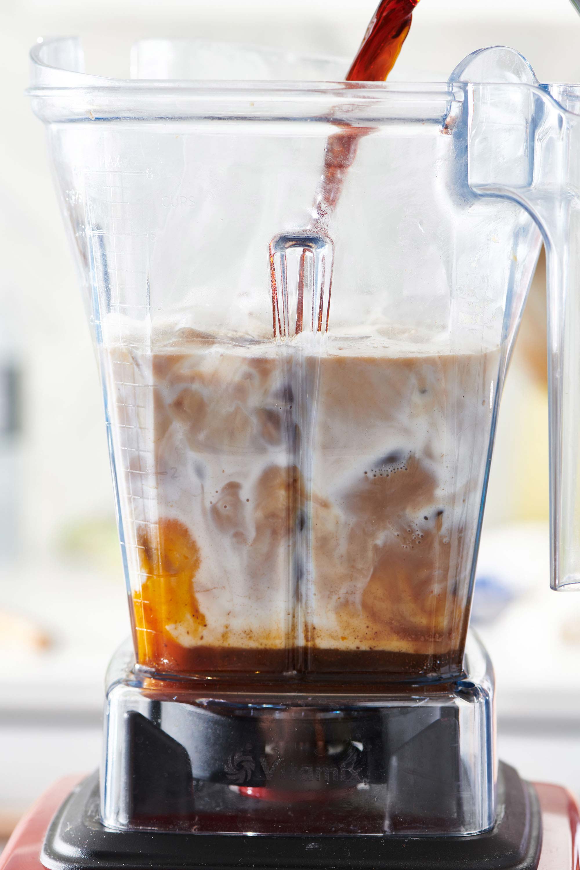 Coffee pouring into a blender with milk and other ingredients.